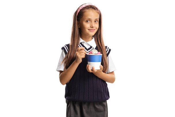 Cute schoolgirl holding ice cream in a paper cup and smiling at camera isolated on white background - Foto, Imagem