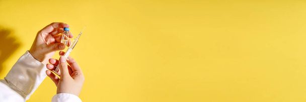 Close-up na mão de mulher branca desconhecida médico segurando seringa com agulha e injeção de vacina na frente da parede amarela - covid-19 coronavírus conceito de vacinação saúde medicina espaço cópia - Foto, Imagem