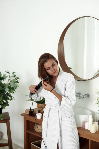 Junge Frau föhnt Haare im Badezimmer. Schönheitsstil - Foto, Bild