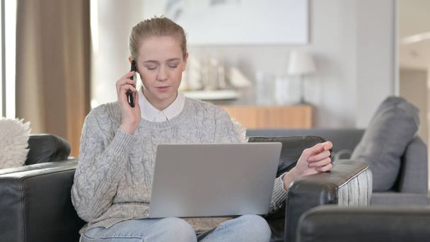 Весела жінка з ноутбуком розмовляє по телефону вдома
 - Фото, зображення