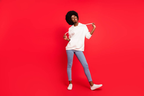 Full body photo of nice brunette millennial lady wear hoodie jeans sneakers isolated on red background - Foto, afbeelding