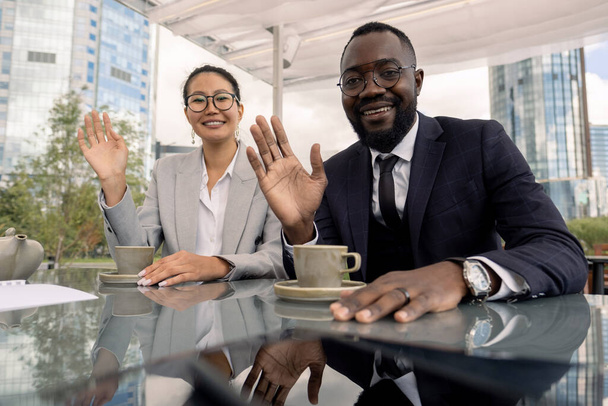 Ασιάτες και Αφρικανοί εργαζόμενοι με λευκό γιακά χαιρετώντας τους συναδέλφους τους κατά τη διάρκεια ηλεκτρονικής συνάντησης - Φωτογραφία, εικόνα