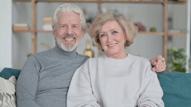 Vecchio coppia seduta su divano e sorridente a camera - Foto, immagini