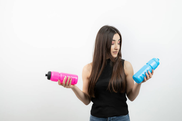 Shot of beautiful sporty woman standing and holding colorful water bottles . High quality photo - Foto, imagen