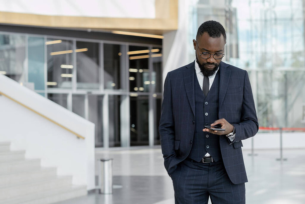 Junger afroamerikanischer Makler im Anzug textet per Smartphone - Foto, Bild