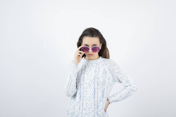 niña usando suéter posando con gafas de sol sobre fondo blanco - Foto, imagen