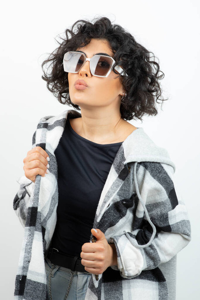Muoti muotokuva nainen kihara tukka poseeraa tyylikäs lasit yli valkoinen seinä. Laadukas kuva - Valokuva, kuva