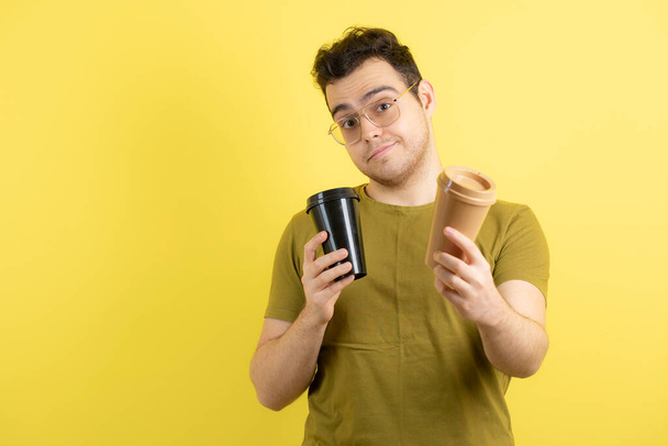 Zdjęcie młodego człowieka w okularach trzymającego filiżankę kawy nad żółtym. Wysokiej jakości zdjęcie - Zdjęcie, obraz