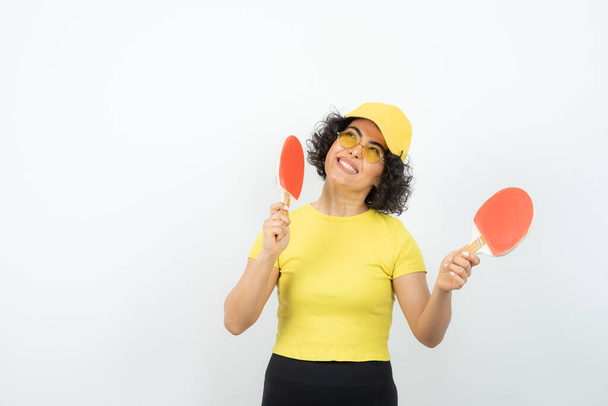 mujer en camiseta amarilla posando sobre fondo blanco con raquetas de ping pong - Foto, imagen