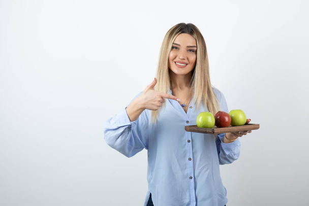 Muotokuva blondi tyttö osoittaa puulauta vihreä ja punainen omenat. Laadukas kuva - Valokuva, kuva