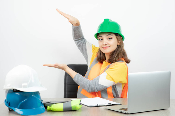 Egy egyenruhás dolgozó nő ül az asztalnál, és kézzel mutatja a méretét. Kiváló minőségű fénykép - Fotó, kép