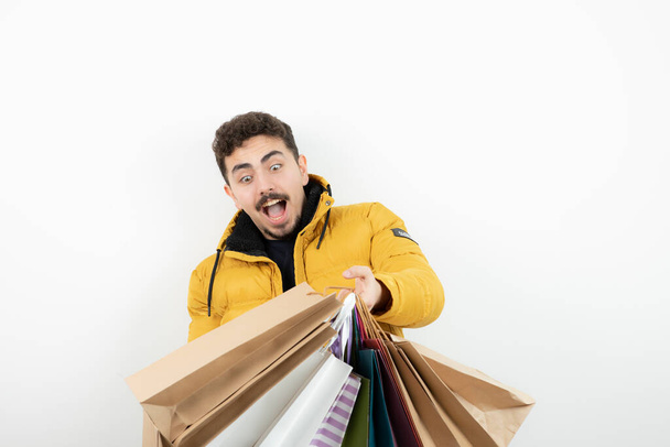 Фото взволнованного бородатого мужчины, держащего в руках много красочных пакетов для покупок. Высокое качество фото - Фото, изображение