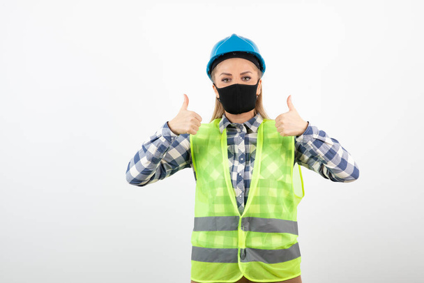 Bauarbeiter in Schutzkleidung mit medizinischer Maske zeigt Daumen hoch. Hochwertiges Foto - Foto, Bild