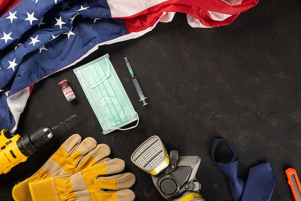 Happy Labor Day. Several engineer constructor work tools, medical face mask protective and American flag with copy space black dark background, American workforce during breakout coronavirus concept - Foto, immagini