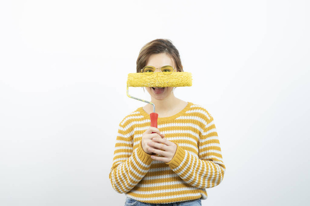 Photo of young woman standing and holding a paint roller in her hand. High quality photo - Photo, Image