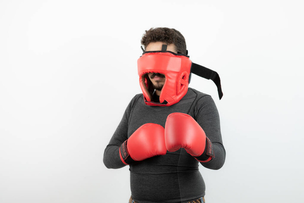 Retrato de un joven con casco de boxeo y guantes sobre una pared blanca. Foto de alta calidad - Foto, Imagen