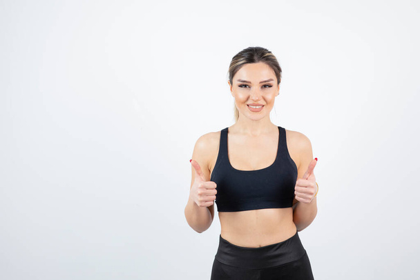 Shot of young attractive woman in sportswear standing and giving thumbs up. High quality photo - Фото, зображення