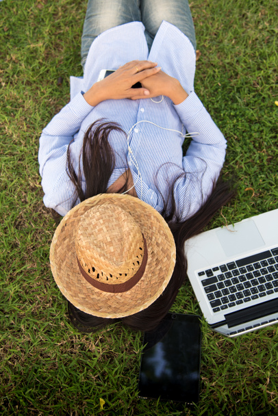 Γυναίκα να κοιμηθεί στο πράσινο γρασίδι λιβάδι κήπο καλοκαίρι ηλιοφάνεια ημέρα ευτυχισμένη στιγμή έξω. Hipster εργασία freelance για laptop χρήση καπέλο κάλυψη πρόσωπο ύπνο στο γρασίδι. Χαλαρώστε Γυναίκα ξαπλωμένη πράσινο κήπο - Φωτογραφία, εικόνα