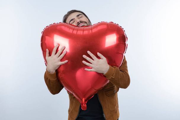 Студийный снимок молодого человека обнимает красный сердечный шар. Высокое качество фото - Фото, изображение