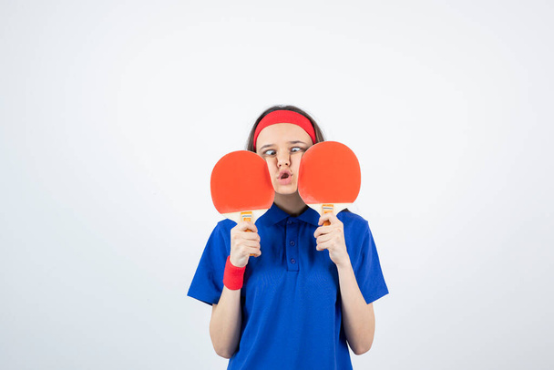 meisje in blauw t-shirt, rode polsband en hoofdband poseren met tennisrackets - Foto, afbeelding