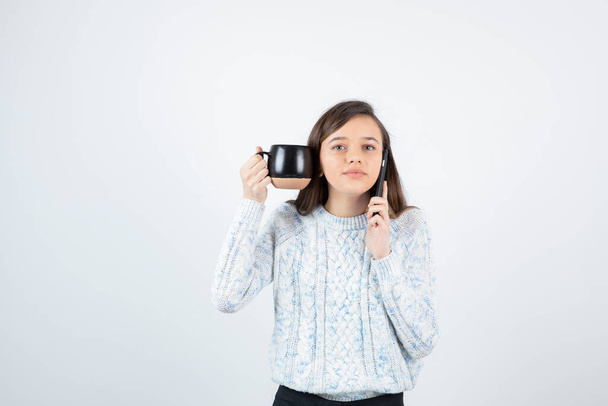 girl wearing sweater posing with cup on white background - Zdjęcie, obraz