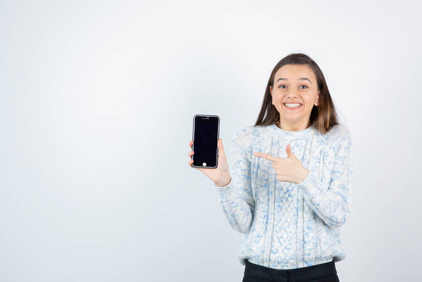 girl wearing sweater posing with smartphone on white background - Foto, Imagen
