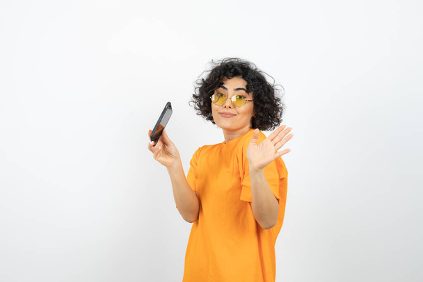 眼鏡をかけた女性とスタジオでスマートフォンを装ったオレンジのTシャツを着た女性 - 写真・画像