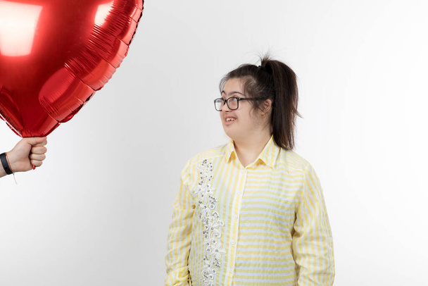 Mädchen mit Down-Syndrom posiert mit rotem Herzballon - Foto, Bild