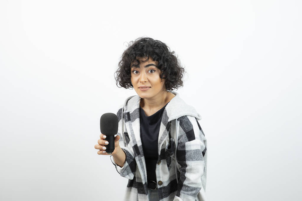 Portret van brunette jonge vrouw met shaggy kapsel holding microfoon. Hoge kwaliteit foto - Foto, afbeelding