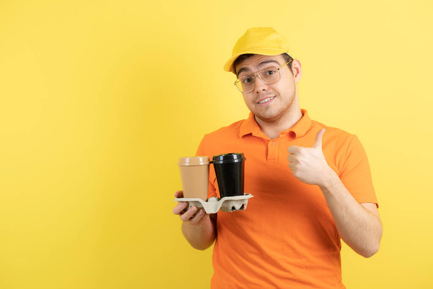 Image d'un jeune homme en uniforme orange tenant des tasses à café à emporter. Photo de haute qualité - Photo, image