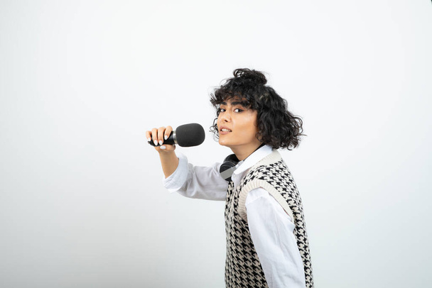 Foto de mujer rizada de pelo corto en auriculares cantando con micrófono. Foto de alta calidad - Foto, Imagen