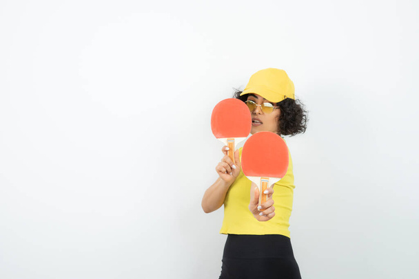 femme en t-shirt jaune posant sur fond blanc avec raquettes ping pong - Photo, image