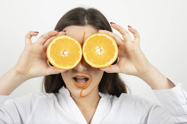 krásná dívka se žlutýma očima a oranžovými vlasy pózuje s citrónem na tváři. - Fotografie, Obrázek