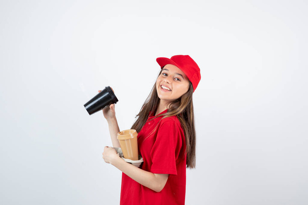 meisje in rood t-shirt en pet poseren met wegwerpbekers - Foto, afbeelding