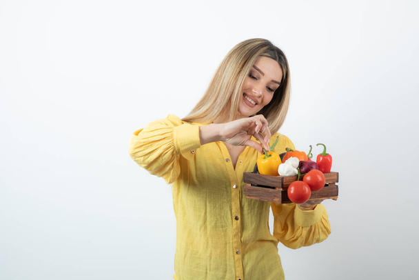 Female farmer standing and holding a wooden crate full of a variety of organic vegetables. High quality photo - Photo, Image