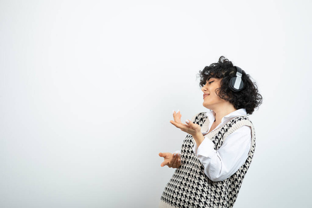 Retrato de una mujer joven de pie y con auriculares en una pared blanca. Foto de alta calidad - Foto, Imagen