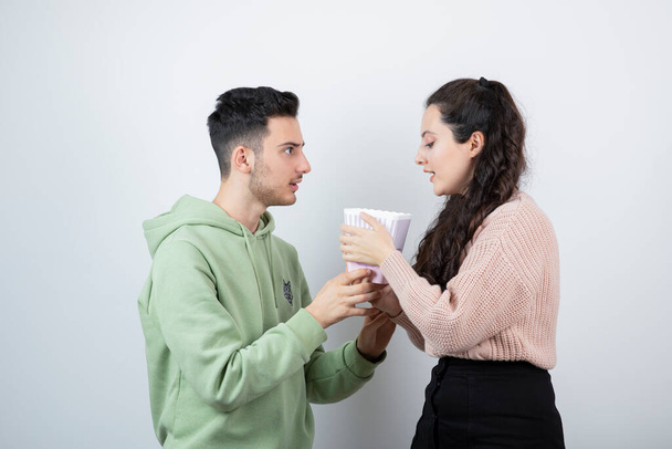 Young couple holding bucket of popcorn against white wall . High quality photo - Photo, Image
