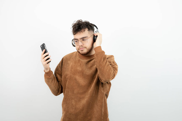 Vonzó férfi zenét hallgat a mobilján keresztül a fehér falon keresztül. Kiváló minőségű fénykép - Fotó, kép