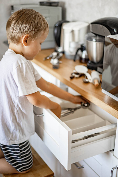 The boy helps his mother in the kitchen to put things in order. Places forks, spoons and cutlery in place. - Valokuva, kuva