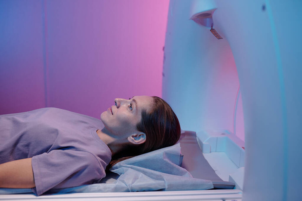 Vista lateral de la mujer joven acostada en la mesa de la máquina de escaneo mri - Foto, Imagen