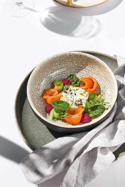 Homemade cheese salad with salmon, cucumber and beetroot. Fancy dinning with salmon salad on white table with simple contemporary decoration. Sunlight and harsh shadow still life. Salmon salad bowl - Fotoğraf, Görsel