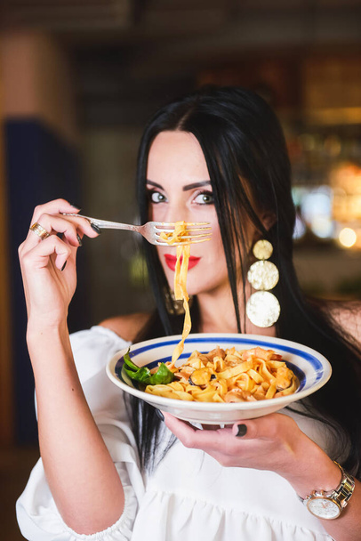 Gorgeous young brunette woman having Italian food. Beautiful woman inside Italian restaurant eating traditional Italian pasta spaghetti. Alone in restaurant, social distancing. Fashion shooting. - Photo, Image