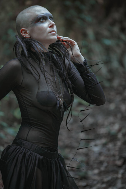 Mystérieuse femme chauve fantôme dans une robe longue noire. Dame païenne gothique près du temple et des idoles. Le vampire marche dans une forêt mystique sombre et profonde. - Photo, image