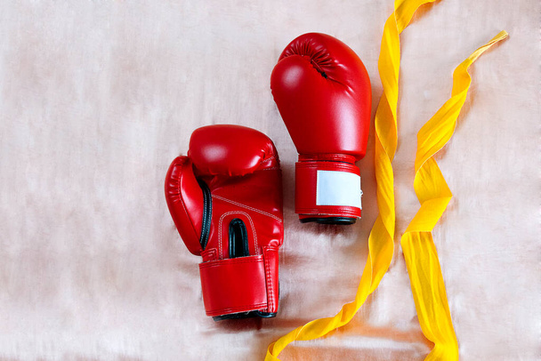 Κόκκινα γάντια πυγμαχίας και κίτρινα περιτυλίγματα πολυεστέρα για muay thai ή αξεσουάρ kickboxing υποστήριξη άρθρωση των χεριών σας σε γυμνό σατέν φόντο - Φωτογραφία, εικόνα