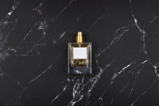 Transparent bottle of perfume with spray on black marble surface. - Zdjęcie, obraz