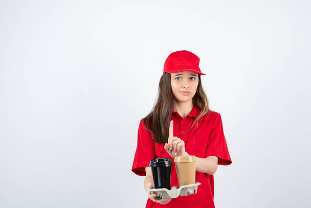meisje in rood t-shirt en pet poseren met wegwerpbekers - Foto, afbeelding