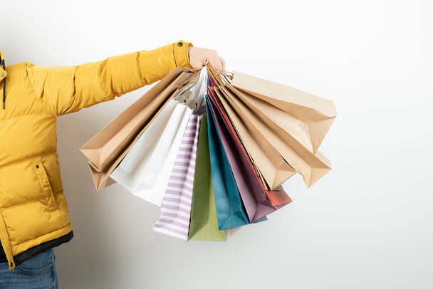 Mão masculina segurando um monte de sacos de compras coloridos sobre uma parede branca. Foto de alta qualidade - Foto, Imagem