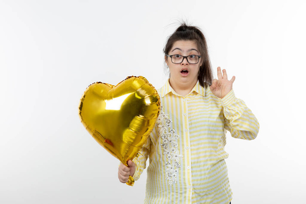 dziewczyna z zespołem Downa pozowanie ze złotym balonem serca - Zdjęcie, obraz