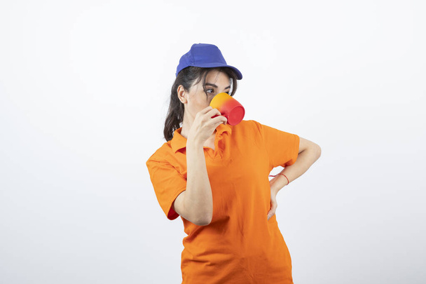 Mujer joven con gorra y uniforme bebiendo de una taza. Foto de alta calidad - Foto, imagen