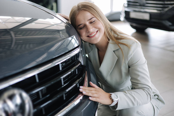 Business woman chossing a new car in a car showroom. Happy female hug new car and very glad - Fotó, kép